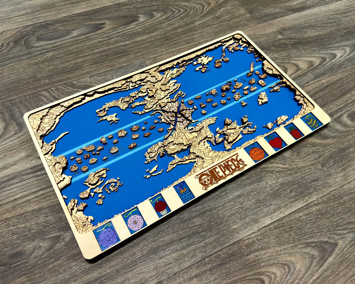 Light birch layered One Piece world map with blue sea and eight fruit panels lying at an angle on a gray wood floor.