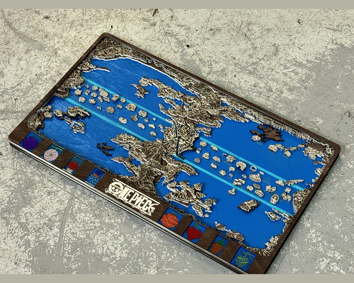 Dark brown and white layered One Piece world map with blue sea and fruit panels lying at an angle on a gray concrete floor.