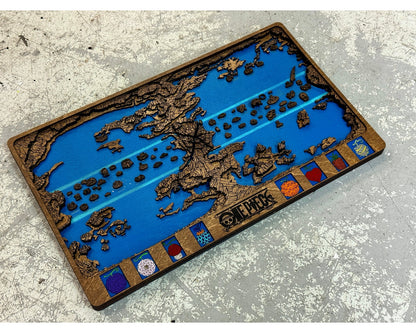 Walnut stained layered One Piece world map with blue sea and eight fruit panels lying at an angle on a gray concrete floor.