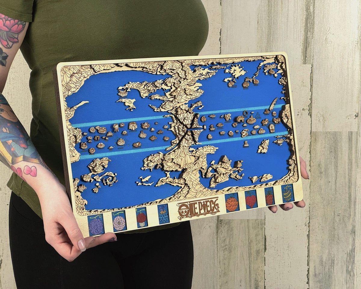 Person in a green top holds a light birch layered One Piece world map with blue sea and fruit panels against pale wood planks.