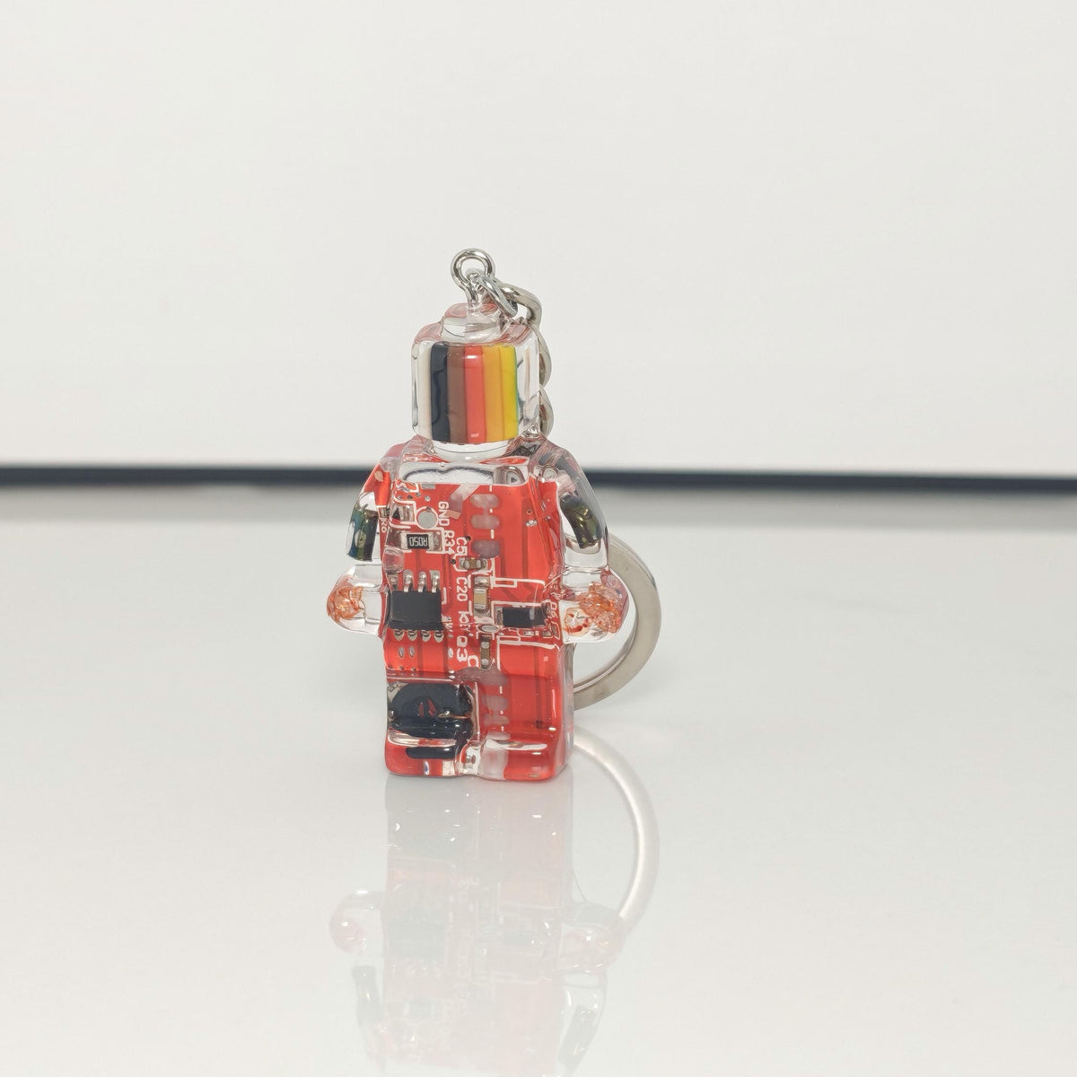 One red circuit board robot keychain with a striped head and silver key ring on a white background
