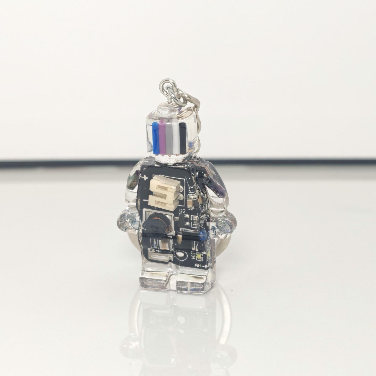 One black circuit board robot keychain with a blue, purple, grey and black striped head on a white background