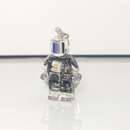 One black circuit board robot keychain with a blue, purple, grey and black striped head on a white background