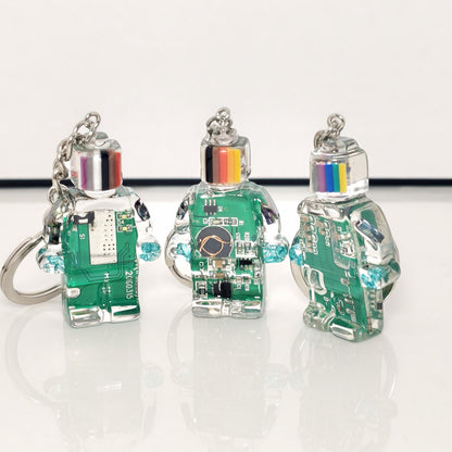 Three green circuit board robot keychains with striped heads and silver key rings on a white surface