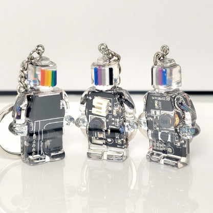 Three black circuit board robot keychains with clear bodies and striped heads on a white surface