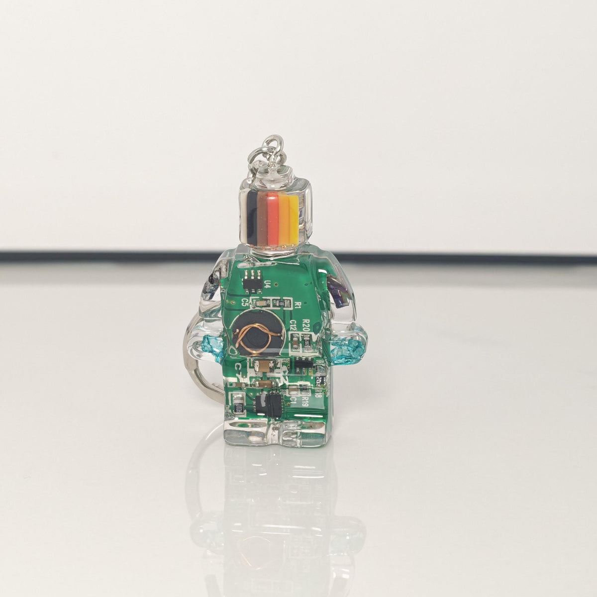 One green circuit board robot keychain with a black, red and yellow striped head on a white background