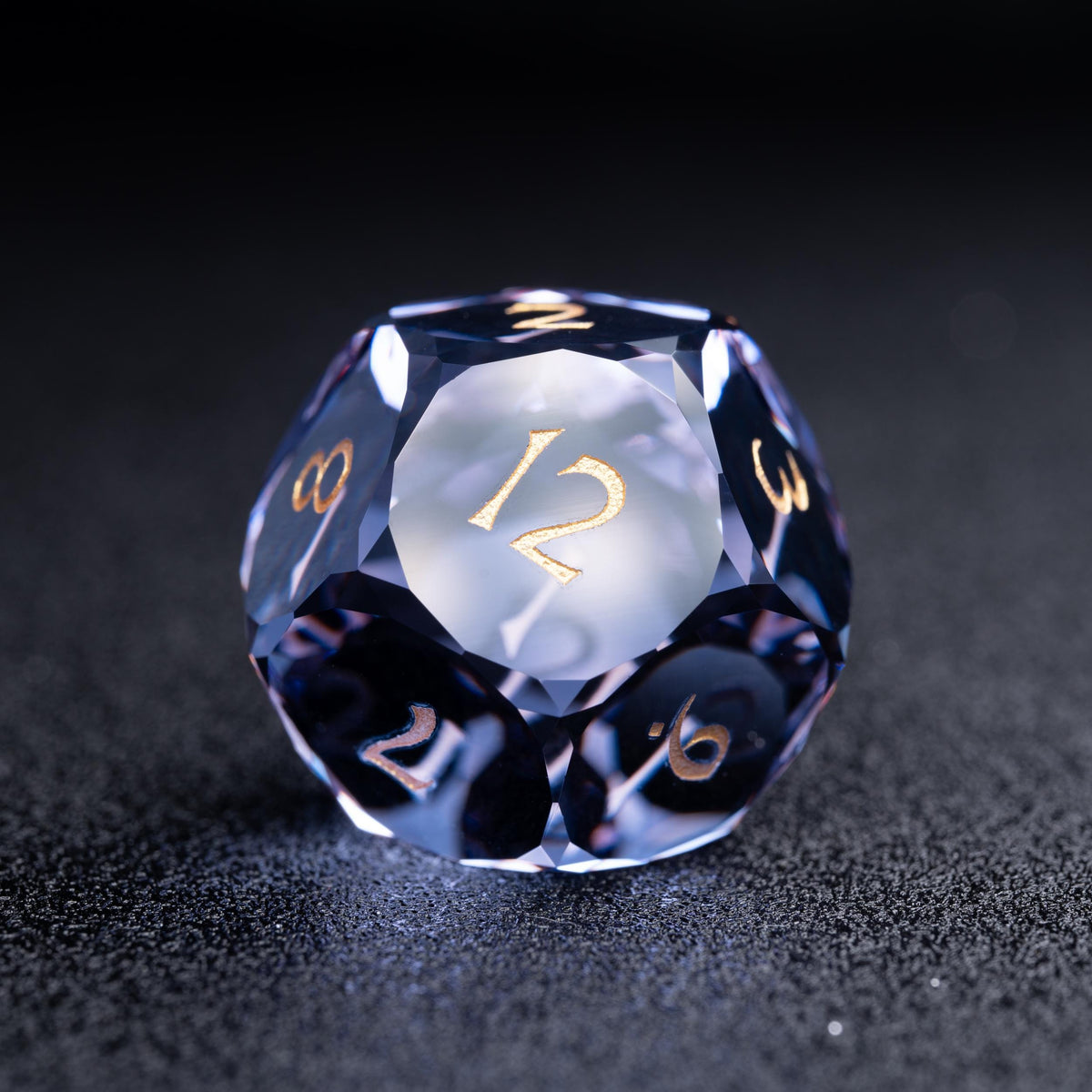 Faceted blue-violet clear d12 die with gold numbers, 12 on the front face, on a dark sparkly surface