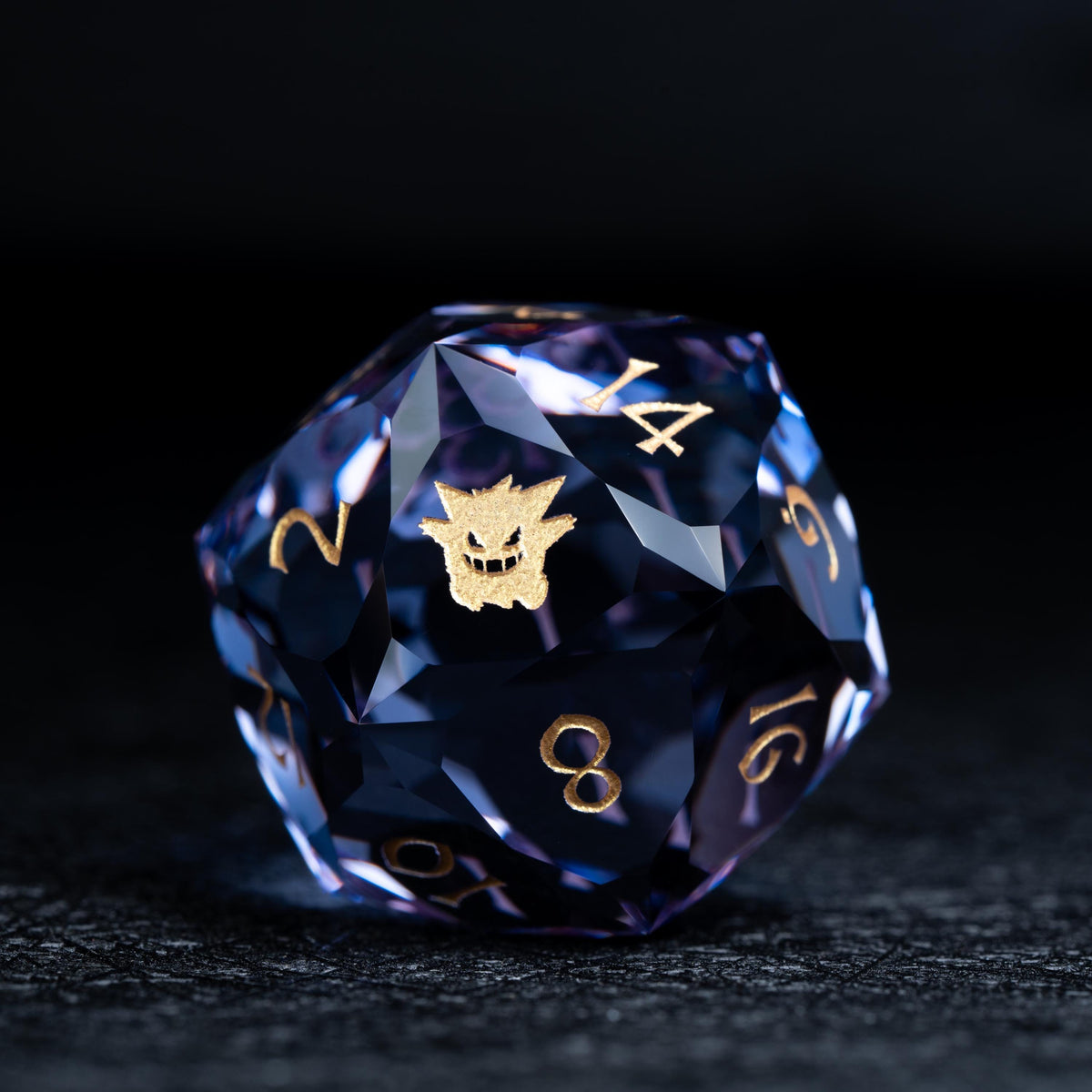 Faceted blue-violet clear d20 die with gold numbers and a gold grinning ghost-like creature symbol on a dark surface