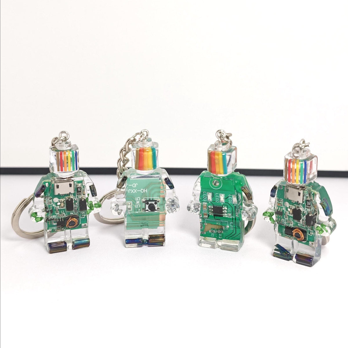 Four green circuit board robot keychains with rainbow-striped heads and silver key rings on a white background