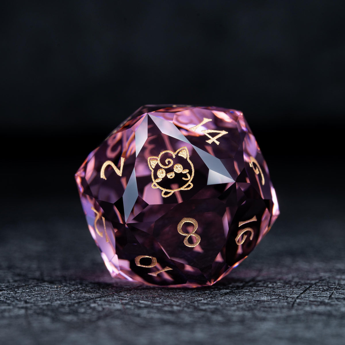 Faceted pink clear d20 die with gold numbers and a gold round curly-haired creature symbol on a dark surface