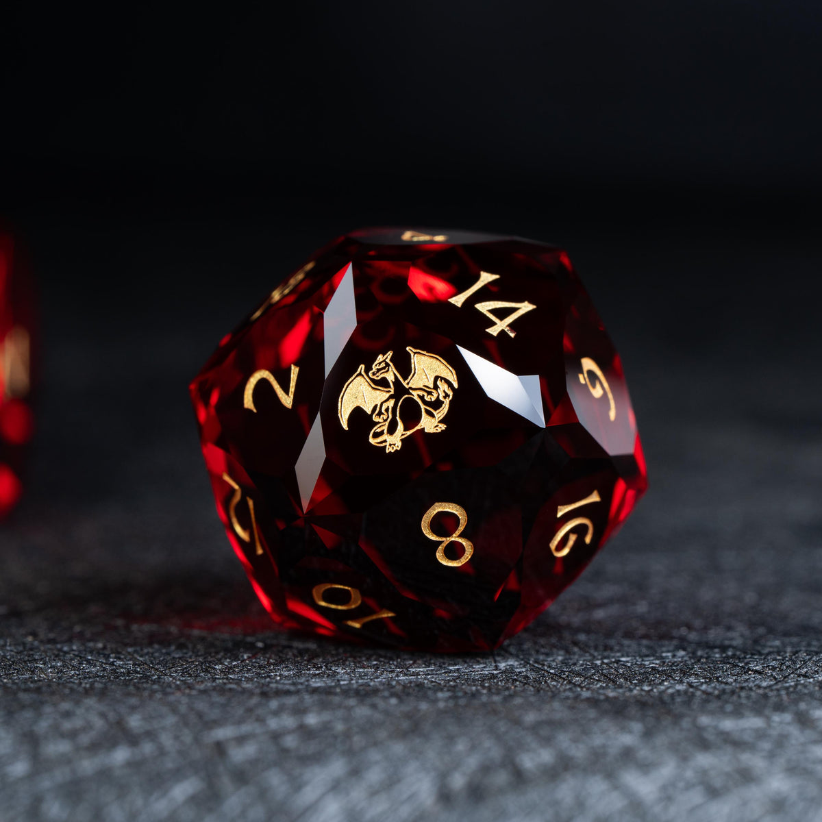 Faceted deep red clear d20 die with gold numbers and a gold winged dragon-like creature on a dark surface