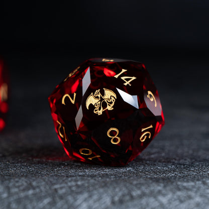 Faceted deep red clear d20 die with gold numbers and a gold winged dragon-like creature on a dark surface